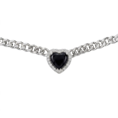 A silver-toned curb chain bracelet featuring a heart-shaped black gemstone surrounded by a halo of small clear stones, set against a plain white background.