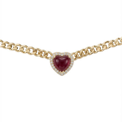 A gold chain necklace featuring a heart-shaped centerpiece with a deep red cabochon gemstone surrounded by a halo of small clear stones, shown against a plain white background.