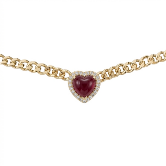 A gold chain necklace featuring a heart-shaped centerpiece with a deep red cabochon gemstone surrounded by a halo of small clear stones, shown against a plain white background.