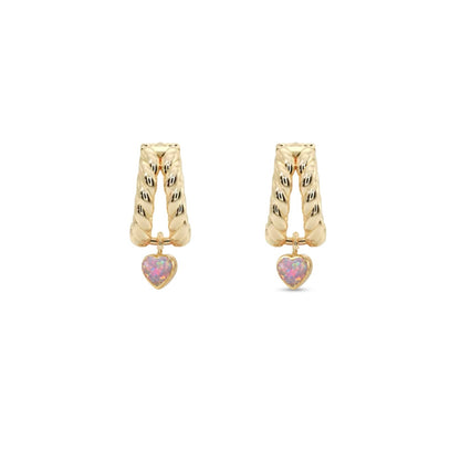A pair of gold huggie hoop earrings with textured vertical bars and a small dangling pink heart charm, shown on a plain white background.