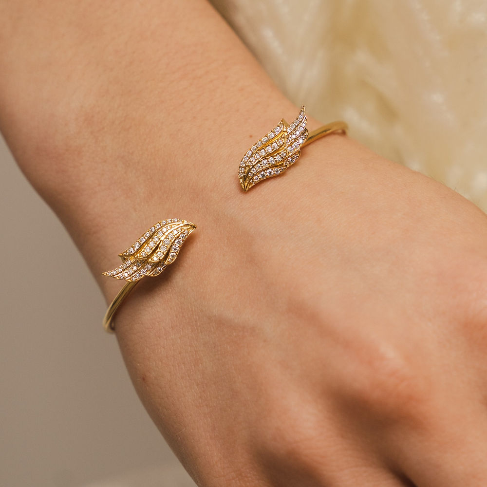 Double Angel Wing Bangle by BLOOMTINE modelled on wrist, crafted from gold over sterling silver and hand-set with brilliant-cut moissanites. A tarnish-resistant, adjustable gold cuff designed as a spiritual talisman, showcasing premium craftsmanship and ethical sparkle
