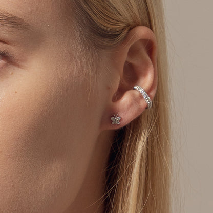 Close-up of a person wearing silver earrings with a neutral background. Small sterling silver butterfly studs by BLOOMTINE with 8 total brilliant-cut lab moissanites. These 5mm dainty, tarnish-resistant earrings are an ethical luxury staple, exclusively available at Wolf & Badger and Rackhams, perfect for birthdays and graduations