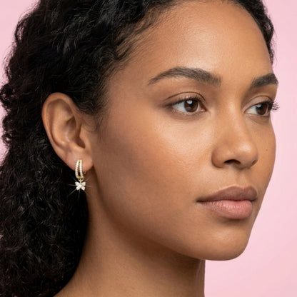 Close-up of a woman wearing a hoop earring with a pink background. BLOOMTINE Flutterfly gold earrings in 14K gold vermeil. Mini gold hoop earrings with moissanite butterfly charms. Tarnish-resistant and meaningful jewelry for transformation