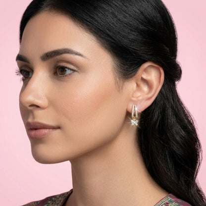 Woman wearing earrings with a pink background. BLOOMTINE Flutterfly gold earrings in 14K gold vermeil. Mini gold hoop earrings with moissanite butterfly charms. Tarnish-resistant and meaningful jewelry for transformation