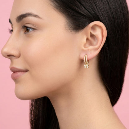 Close-up of a woman wearing gold hoop earrings with a pink background. BLOOMTINE Flutterfly gold earrings in 14K gold vermeil. Mini gold hoop earrings with moissanite butterfly charms. Tarnish-resistant and meaningful jewelry for transformation