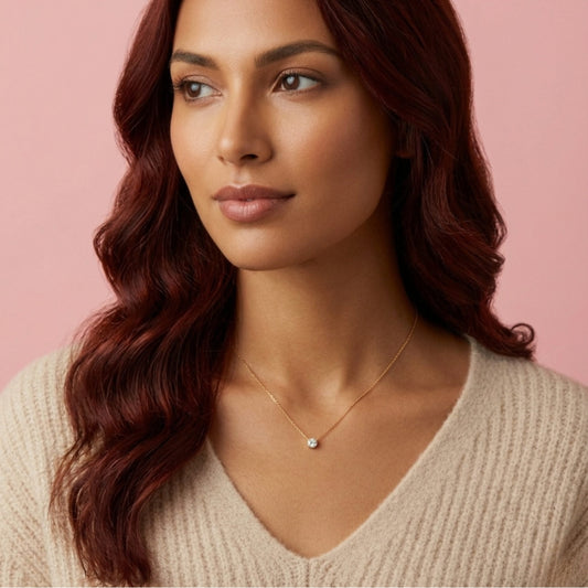 Close-up of a delicate BLOOMTINE gold pendant necklace on a model. This minimalist goddess-inspired accessory features a small, captivating charm on a fine gold-over-silver chain, demonstrating tarnish-resistant everyday luxury against a soft neutral backdrop
