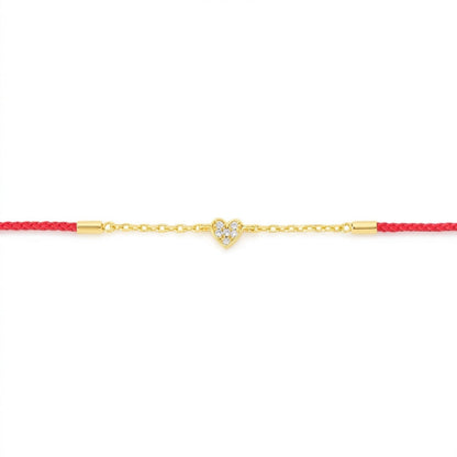 A delicate gold chain bracelet featuring a small heart-shaped charm paved with clear stones, suspended on a vibrant red cord with gold end caps, set against a plain white background.